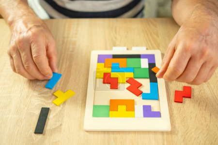 male hand manipulates colorful wooden puzzle, elderly old man composing geometric shapes, brain health and mental well-being, preventing dementia and Alzheimer's disease
