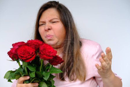 Blumenstrauß, rote Rosen, Frau mittleren Alters 50 Jahre alt mit prallen Augen vor Verwirrung und Überraschung, Unzufriedenheit mit Geschenk, Blütenpollenallergie, emotionales Frauenporträt aus nächster Nähe