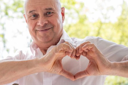 Photo for Mature charismatic 65-year-old man, Loving senior making heart shape with fingers, Tenderness and care, expressing love and affection - Royalty Free Image