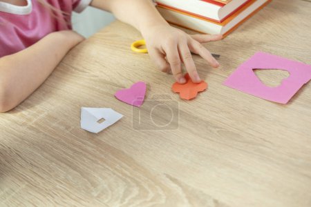 niña preescolar practicando habilidades de tijera cortando formas tales como casa, corazón y flores para apliques de papel de color