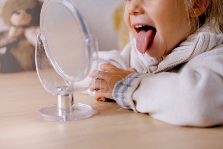 small child front mirror, blonde girl of 4 years old engaged with speech therapist, gymnastics for tongue, defect, speech disorder with frequent repetition sounds, syllables, spasms muscles apparatus