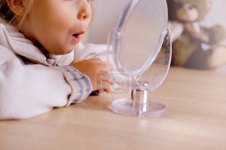 small child front mirror, blonde girl of 4 years old engaged with speech therapist, gymnastics for tongue, defect, speech disorder with frequent repetition sounds, syllables, spasms muscles apparatus