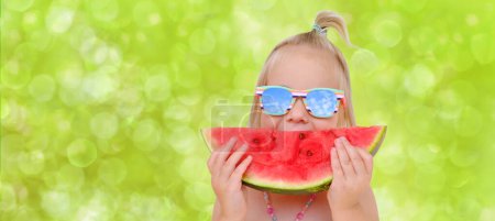 close-up happy cool trendy funky hipster blonde girl in sunglasses eating ripe red watermelon, juicy slice in hands child, toddler, smiling joyfully, green background, happy childhood, life beautiful