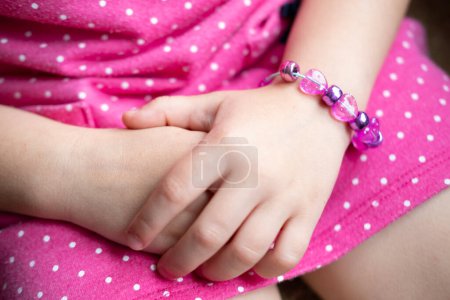 girl's hands with bracelet Close-up, dressed in pink polka dot dress, making personalized bracelet with colorful beads, capturing charming and delicate moment