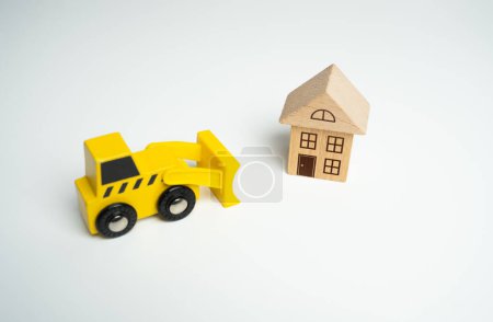 Photo for Yellow toy bulldozer and a house. Encroachment on private property. Illegal buildings and construction. Violation of building codes. Demolition process. - Royalty Free Image
