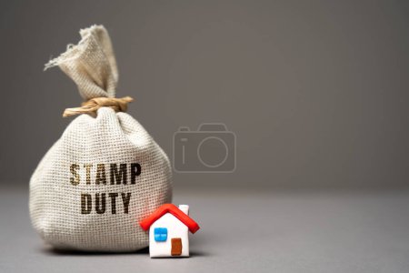 Photo for Stamp duty concept. Taxes assessed during the transfer of real estate between two parties. Buying housing and land. Property. Stamp Duty Land Tax SDLT. Money bag and house - Royalty Free Image