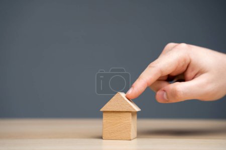Foto de El hombre señala una casa en miniatura. El concepto de bienes raíces y vivienda asequible. Tasas hipotecarias y préstamos. Venta, compra y alquiler de apartamentos. Impuestos, servicios públicos y seguros - Imagen libre de derechos