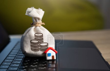 House and a money bag and on the computer keyboard. Make a deal. Property Insurance. Taxes. Community budget. Financial support. Housing stock and infrastructure. Profit. Real estate investment.