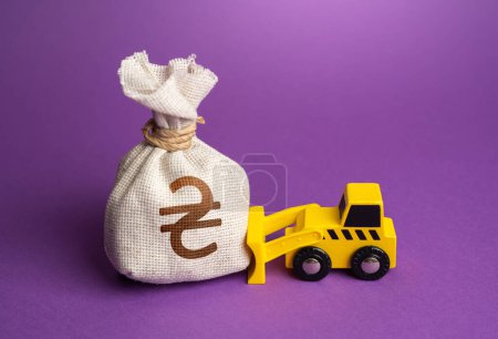 Photo for A bulldozer pushes a ukrainian hryvnia money bag. Financing of dismantling works. Demolition services, land leveling. Industry machinery for rent. Money down the drain. Ineffective use of funds. - Royalty Free Image