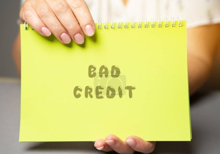 Photo for The inscription Bad credit in a notepad. Credit and loan concept. Business and finance. Woman's hand holding a notepad - Royalty Free Image