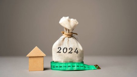 Wooden house and money bag 2024. Family budget planning for next year. Investments, plans, savings. Mortgage rates. Real estate concept. Refinance home.