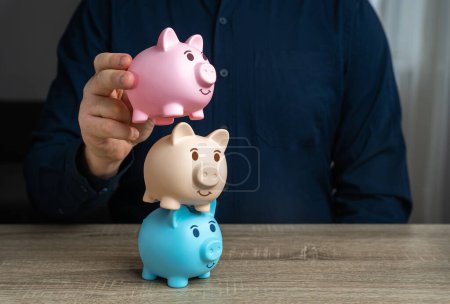 A businessman builds a tower from piggy banks. Multiple deposits. Savings and deposit banking. Healthy economy. Diversification of investments and savings. Banking. Good conditions from the bank.