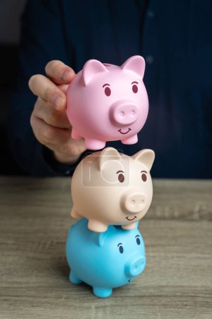 Photo for A businessman builds a tower from piggy banks. Savings and deposit banking. Multiple deposits. Healthy economy. Diversification of investments and savings. Banking. Good conditions from the bank. - Royalty Free Image