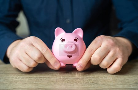 Photo for A man holds a funny pig piggy bank. Wealth and prosperity. Savings and deposit banking. Healthy economy. Successful investments and deposits. - Royalty Free Image