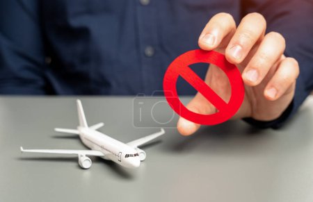 Photo for A man holds a prohibitory sign near an airplane. Sanctions. Refusal of aircraft insurance, breaking leasing agreements. Closing air routes. Flight cancellation. Failure safety tests. Restrictions - Royalty Free Image
