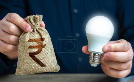 Foto de Rupia india bolsa de dinero y la quema de bombilla idea en las manos de un hombre. Ofrecer incentivos financieros para mejorar la eficiencia energética. Reducir la huella de carbono. Inversión en una idea. - Imagen libre de derechos