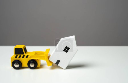 Un bulldozer démolit une maison. Chiffres de jouets. Service de nettoyage de territoire. Le bulldozer veut démolir la maison. Faire place aux développements futurs.