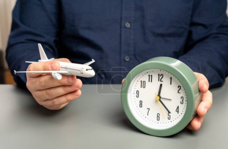 Un hombre sostiene un avión de pasajeros y un reloj. Tiempo de vuelo. Planificación de una ruta con traslados.