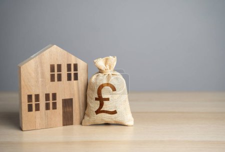 Wooden house figure and british pound sterling money bag. Taxes. Property value appraisal. Make a deal. Housing prices. Buying and selling real estate. Property Insurance.