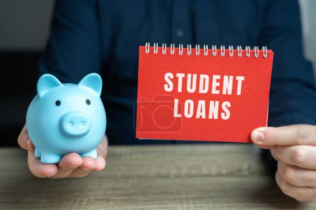 Student loans concept. Financial aid provided to students to help cover the cost of higher education. Note in male hands and pig piggy bank
