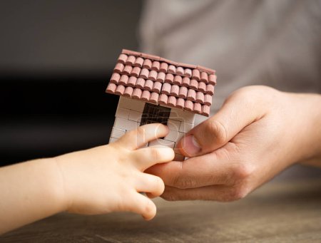Un padre le da a su hijo una pequeña casa. El concepto de transferencia de propiedad y herencia. Bienes raíces. vivienda como regalo, apartamento o casa