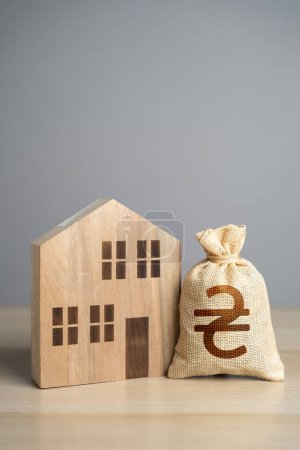 Wooden house figure and ukrainian hryvnia money bag. Taxes. Property value appraisal. Make a deal. Buying and selling real estate. Property Insurance. Housing prices.