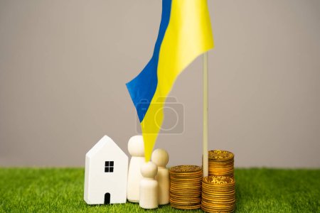 Le concept d'aider les résidents ukrainiens touchés par la guerre. Soutien financier et dons. Une famille se tient près d'une maison, des pièces de monnaie et du drapeau de l'Ukraine. Budget