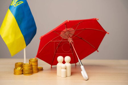 Le concept d'aider les résidents ukrainiens touchés par la guerre. Soutien financier et dons. Un couple marié se tient sous un parapluie près des pièces de monnaie et le drapeau de l'Ukraine.
