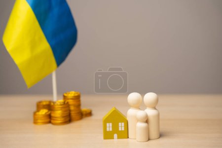 Le concept d'aider les résidents ukrainiens touchés par la guerre. Soutien financier et dons. Une famille se tient près d'une maison, des pièces de monnaie et du drapeau de l'Ukraine. Budget