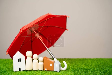 Sach- und Familienversicherungskonzept. Miniaturfiguren einer Familie stehen neben einem Haus und einem roten Regenschirm. Sicherheitsleben