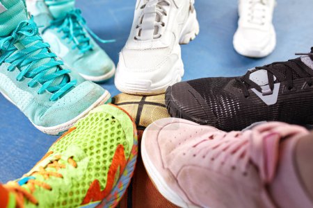 Photo for Bright and colorful sport shoes circle with basket ball top view. Set of different sneakers on blue floor, copy space. Team game, competition concept. - Royalty Free Image