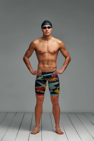 Retrato de un nadador con gorra y máscara, retrato de cuerpo entero, joven nadador atleta con gorra y máscara para nadar, copias del espacio, fondo gris.