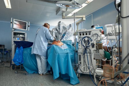 Foto de Llevar a cabo una operación con un robot, un robot cirujano con manipuladores, un quirófano moderno, cirujanos personas realizan una operación con un robot cirujanos a través del panel de control - Imagen libre de derechos