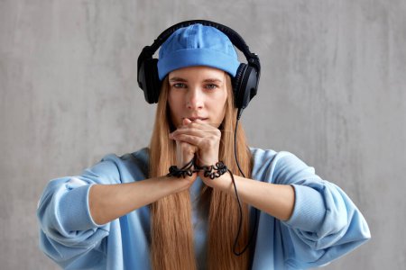 Téléchargez les photos : Une jeune femme charmante aux cheveux roux, vêtue d'un pull bleu et coiffée d'un casque DJ sur la tête, a plié les mains dans une pose de prière. Musique et méditation - en image libre de droit