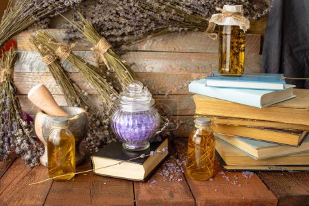 Libros antiguos, flores secas de lavanda y botellas de aceite esencial sobre fondo de madera.