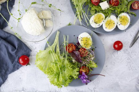 Téléchargez les photos : Salade saine avec laitue, tomates cerises, fromage mozzarella et microgreens, sur une assiette, fond clair - en image libre de droit