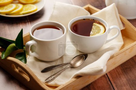 Tee für zwei. Schwarzer Tee in weiß, Keramiktassen. Hölzerner Hintergrund.