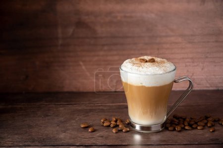 Glass cup of layered coffee drink with milk foam, wooden background and copy space.