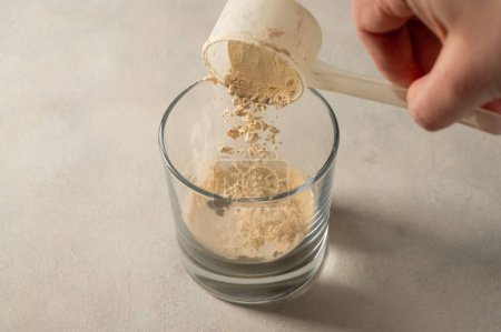 Photo for Pouring protein powder from scoop, in glass a glass. Making protein drink - Royalty Free Image
