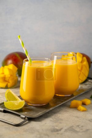 Mango smoothie in a glass with fresh mango on background