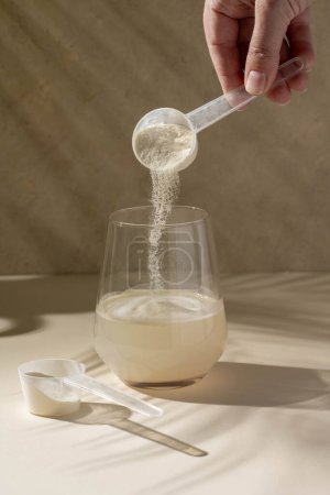 Téléchargez les photos : Poudre de protéines ajoutée avec une cuillère à mesurer dans un verre d'eau. Nutrition et complément alimentaire. - en image libre de droit