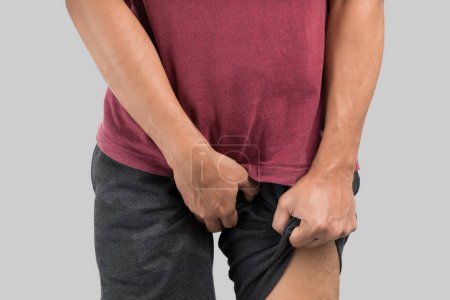 Asian men grab or cover his crotch because wanting to urinate against gray background.