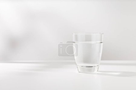 Reines Wasser im Glas steht auf dem weißen Holztisch.