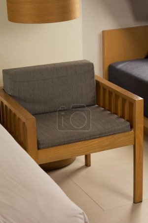 Depicted herein is an elegantly appointed chamber, featuring a wooden chair with a grey cushion, strategically positioned adjacent to a bed and circular table. The room exudes an atmosphere of tranquility and sophistication, further enhanced by the h