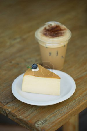 Ein verführerisches Stück cremiger Käsekuchen gepaart mit einem erfrischenden Eiskaffee auf einem rustikalen Holztisch.