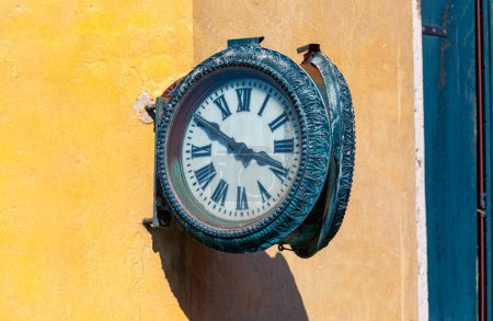 Téléchargez les photos : Ancienne horloge de rue ronde est monté sur un mur jaune altérée. Horloge dans une rue charmante dans une ville européenne pittoresque - en image libre de droit