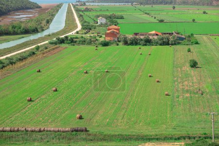 Paisaje rural con pajar en el campo y pueblo en el fondo. Maravillosas tierras de cultivo en primavera. Campos agrícolas verdes en Croacia