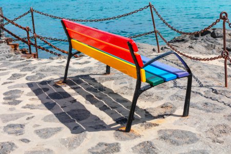 Colorful bench on the coast. Multicolored wooden seat on the cobblestone shore