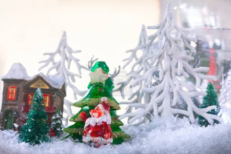 Weihnachtsbaum mit Weihnachtsmann auf Schnee und Haus Hintergrund. Weihnachten im Spielzeugwunderland