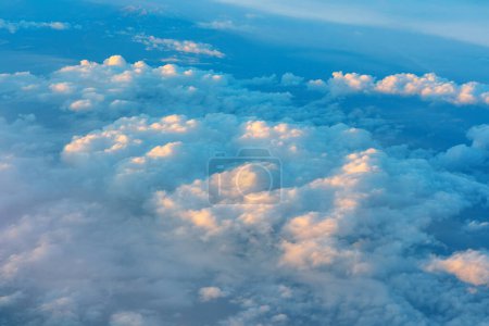 Fluffy clouds drifting across expanse blue sky. View through window of an aircraft